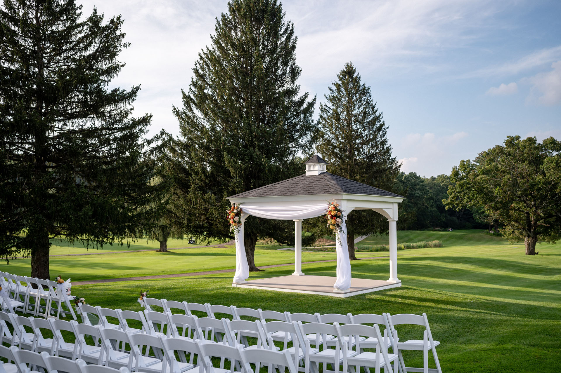 Beautiful outdoor wedding venue with verdant rolling hills and florally-adorned gazebo.